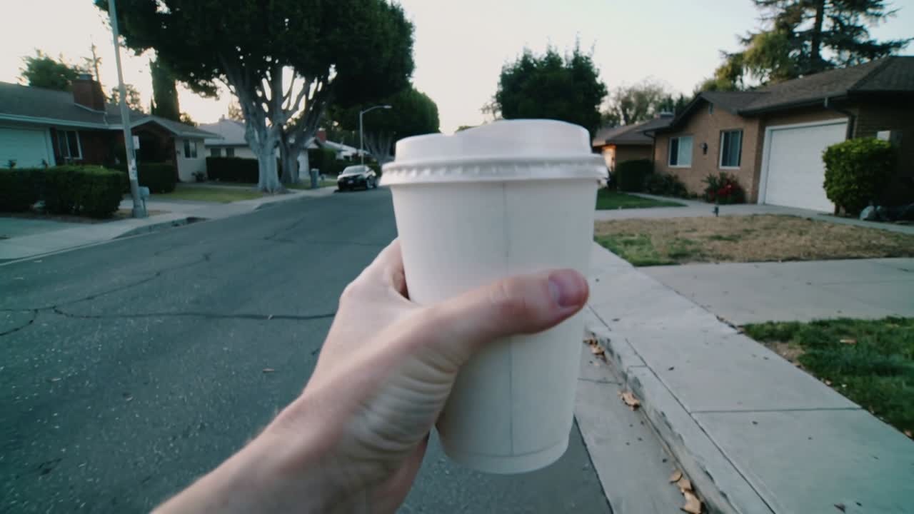 Person holding white cup with lid and releasing bag strap while walking suburban street for health