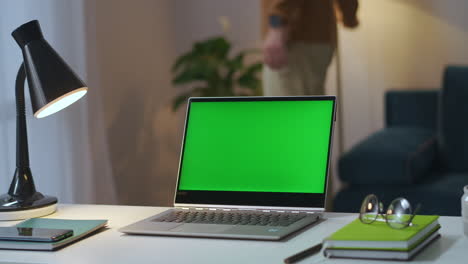 Cuaderno-Con-Pantalla-Verde-En-La-Mesa-De-Trabajo-En-La-Oficina-En-Casa-El-Hombre-Está-Apagando-Las-Lámparas-De-Mesa-Y-De-Pie-En-La-Sala-De-Estar-Y-Cerrando-La-Tecnología-De-Clave-Cromática-De-La-Cubierta