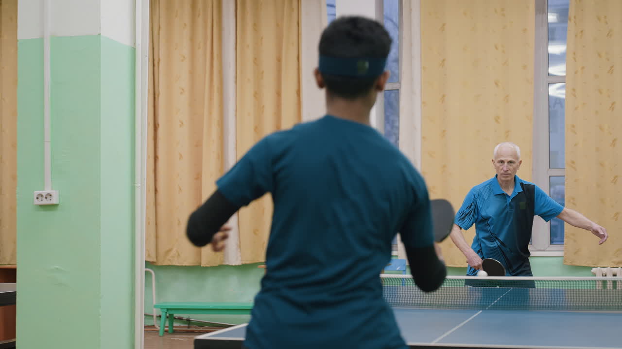Focused table tennis training session indoors with senior coach rallying against young player across net highlighting practice discipline mentorship