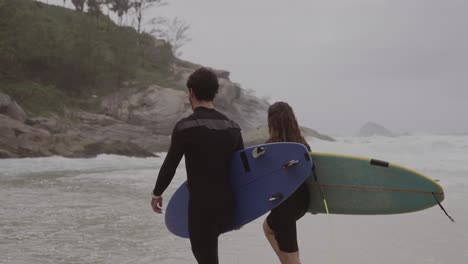 couple walking on beach with surfboards towards the ocean