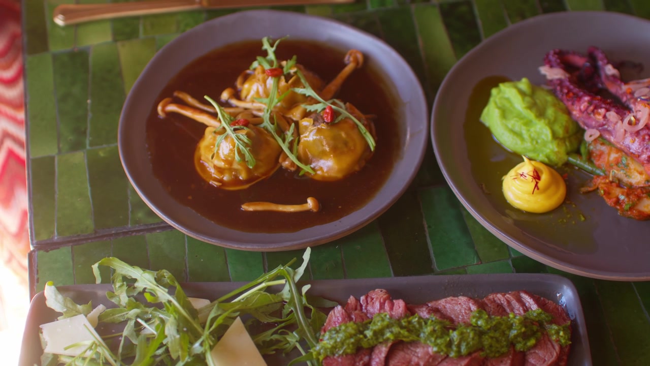 Platos gourmet variados servidos en una mesa de azulejos verdes en un ambiente de restaurante de Marrakech.