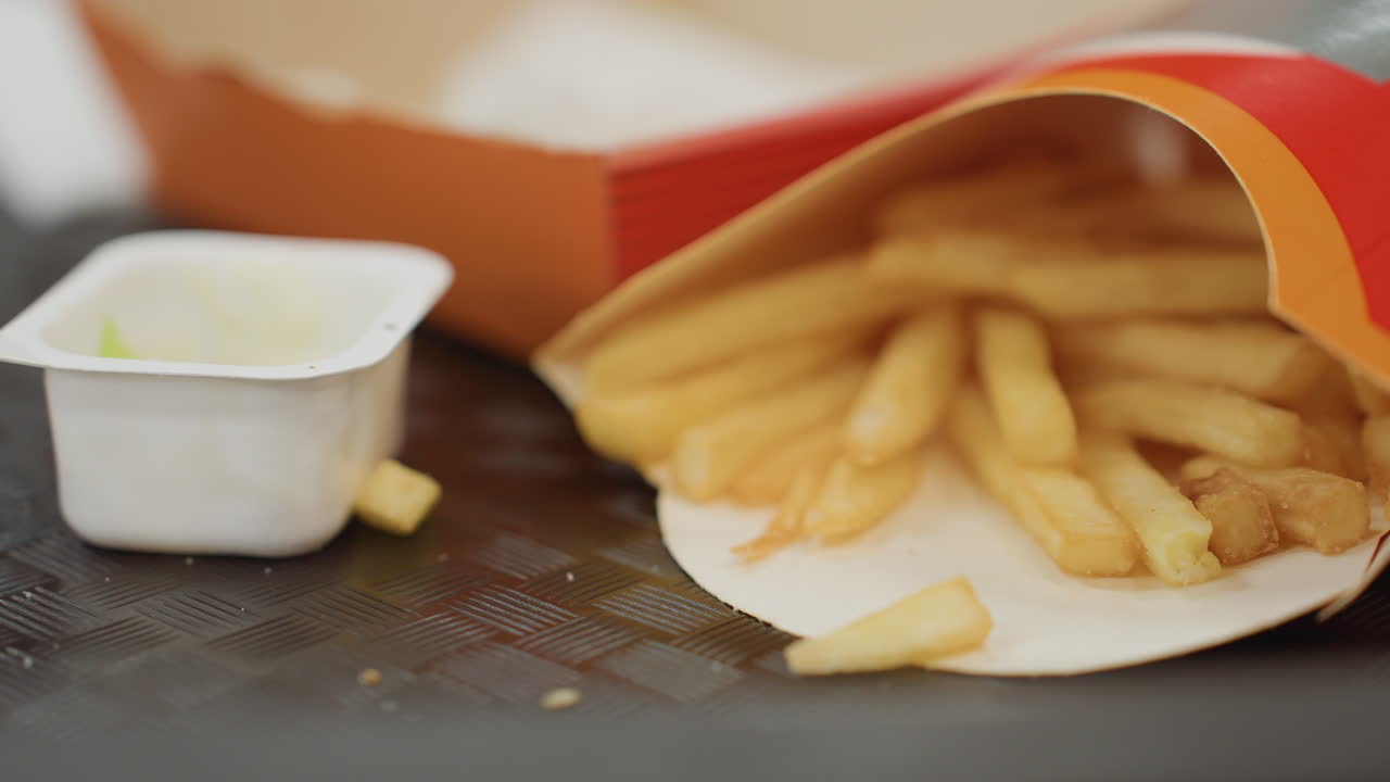 바삭한 감자를 고르는 손, 매니큐어를 칠한 손톱과 감자튀김 클로즈업, 양념된 감자칩과 소스를 곁들여 스낵을 즐기는 학생, 양념된 감자튀김을 고르는 손이 있는 편안한 푸드코트 풍경