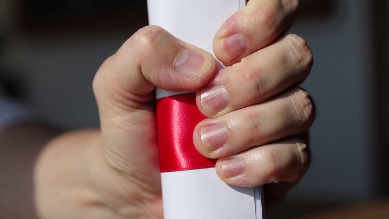Daumen drückt, rechte Hand festigt den Griff, um gerolltes weißes Papier in einem Raum mit rotem Satinband zu fixieren.