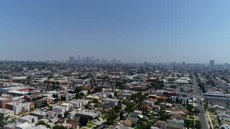 static drone aerial shot over los angeles neighborhood with rooftops, blue skies and downtown la in the background