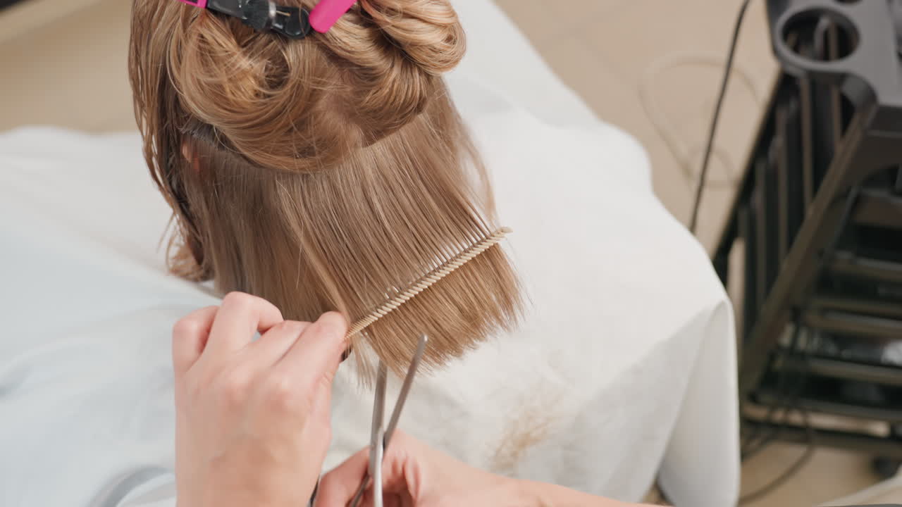 Parrucchiere che realizza un taglio di capelli strutturato e a strati, vista posteriore dei capelli della cliente divisi con clip, parrucchiere che pettina e taglia la frangia, polvere di capelli sottili che cade, strumenti sul carrello, atmosfera vivace del salone