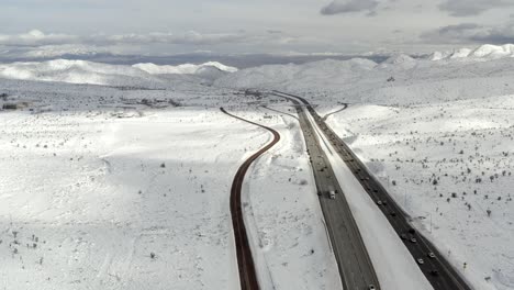 aerial, drone shot, overlooking traffic on interstate 15, on a mountain pass, surrounded by snowy peaks, on a sunny, winter day, in california, near nevada, usa