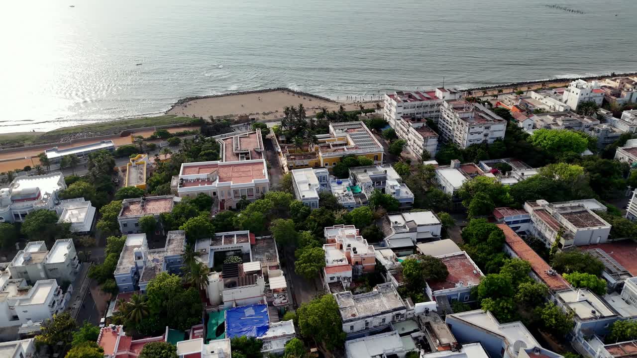 Riprese aeree di una vivace città costiera, Pondy. L'inquadratura mostra una spiaggia sabbiosa con barche da pesca accanto a una comunità densamente popolata di edifici colorati, offrendo una vista unica della vita di mare