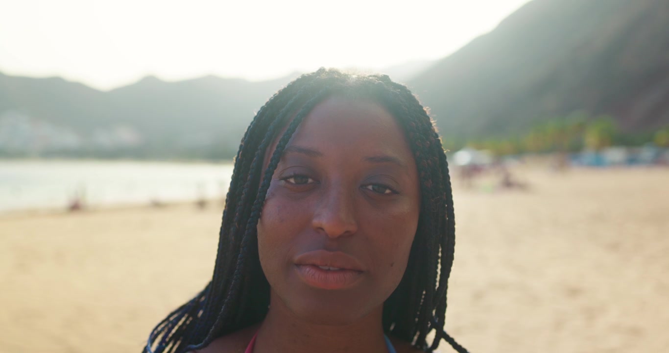 Portræt af en ung afroamerikansk kvinde med fletninger på en solrig strand
