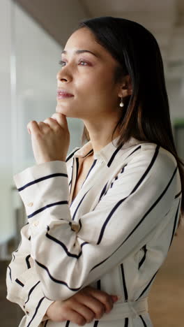 vertical video: confident businesswoman in striped shirt standing in modern office setting