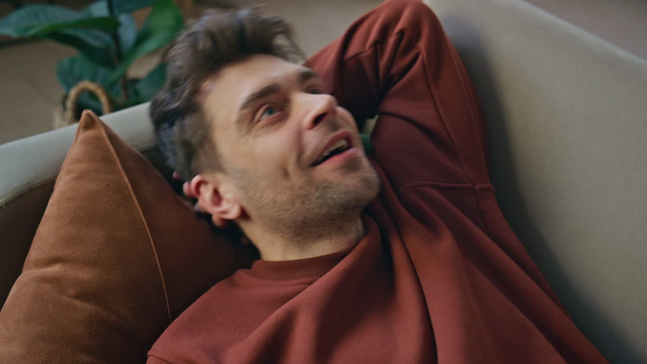 Smiling guy lying couch with smartphone taking rest after work day close up.