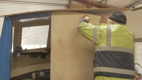 shipwright secures bolts on new plywood bulkhead in fiberglass boat