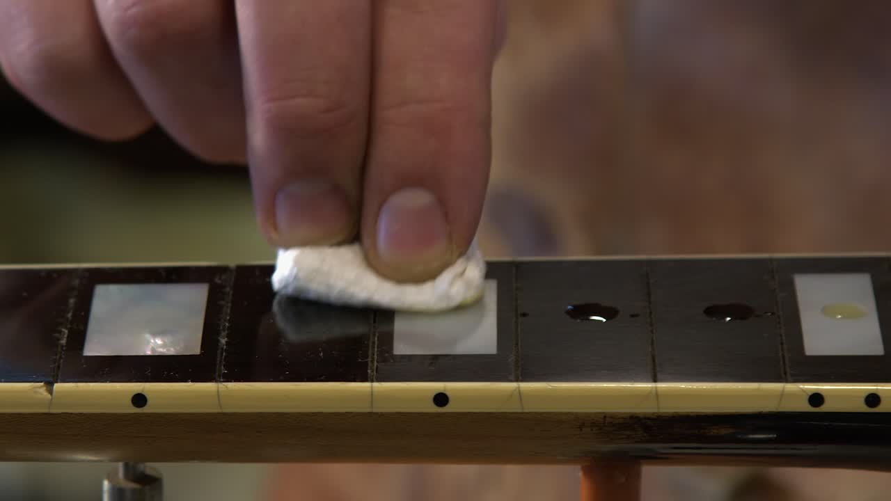 Panning shot as guitar tech rubs oil into ebony fretboard, closeup
