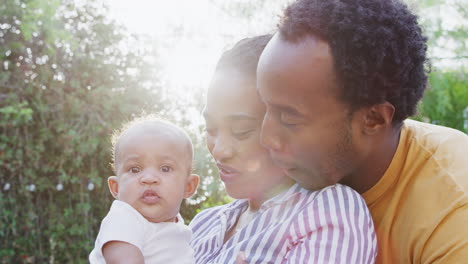 Portrait-Of-Loving-Parents-Holding-Baby-Daughter-At-Home-Outdoors-In-Garden