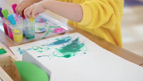 little kid drip painting holding droppers in both hand and spreading watercolors on paper - hands close-up