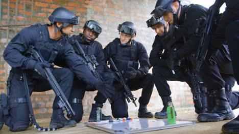 Side-view-of-mixed-race-military-soldiers-with-rifles-planning-and-crouching-on-floor-at-base-4k