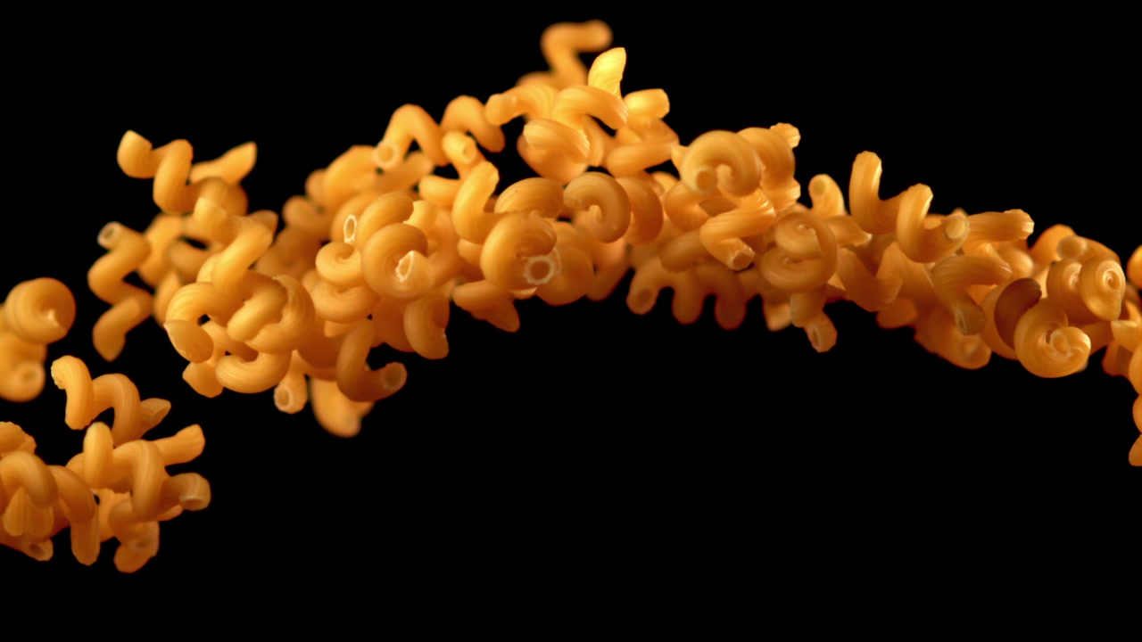 Pasta fusilli dorata che galleggia e cade su sfondo nero.