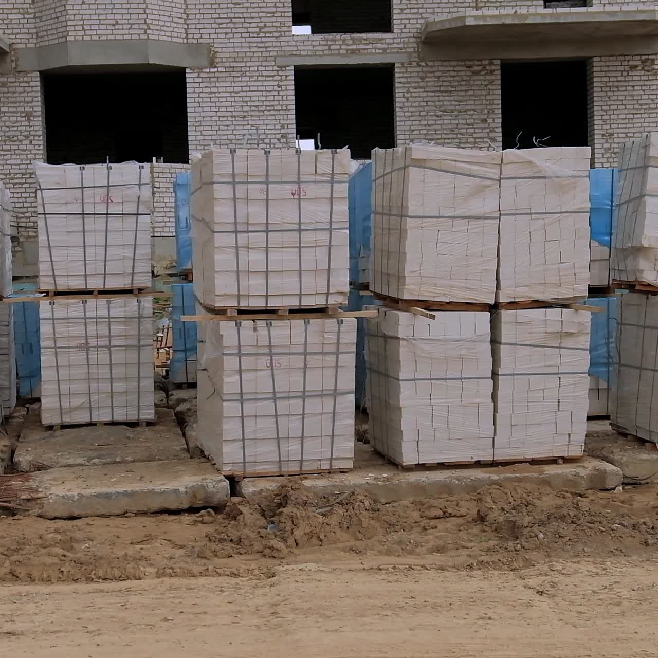 Building site with white bricks prepared for house construction. Unfinished buildings and a crane at backdrop