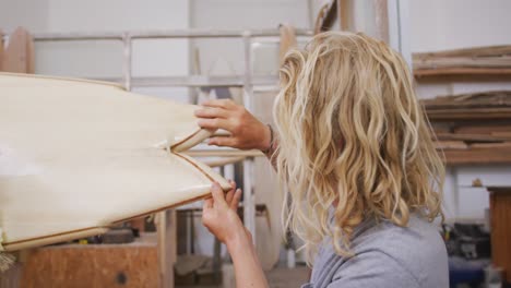 a caucasian male surfboard maker polishing a wooden surfboard edge