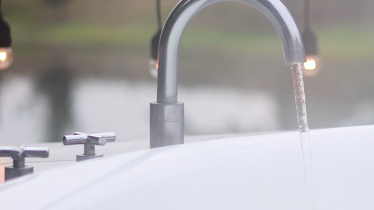 A detailed view of water streaming from a shiny metal faucet with a blurred natural background.