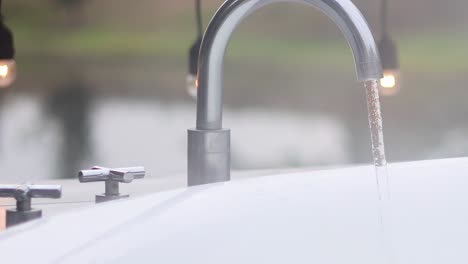 a detailed view of water streaming from a shiny metal faucet with a blurred natural background.