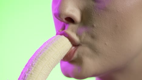 mujer joven comiendo un plátano, boca de primer plano, fondo verde