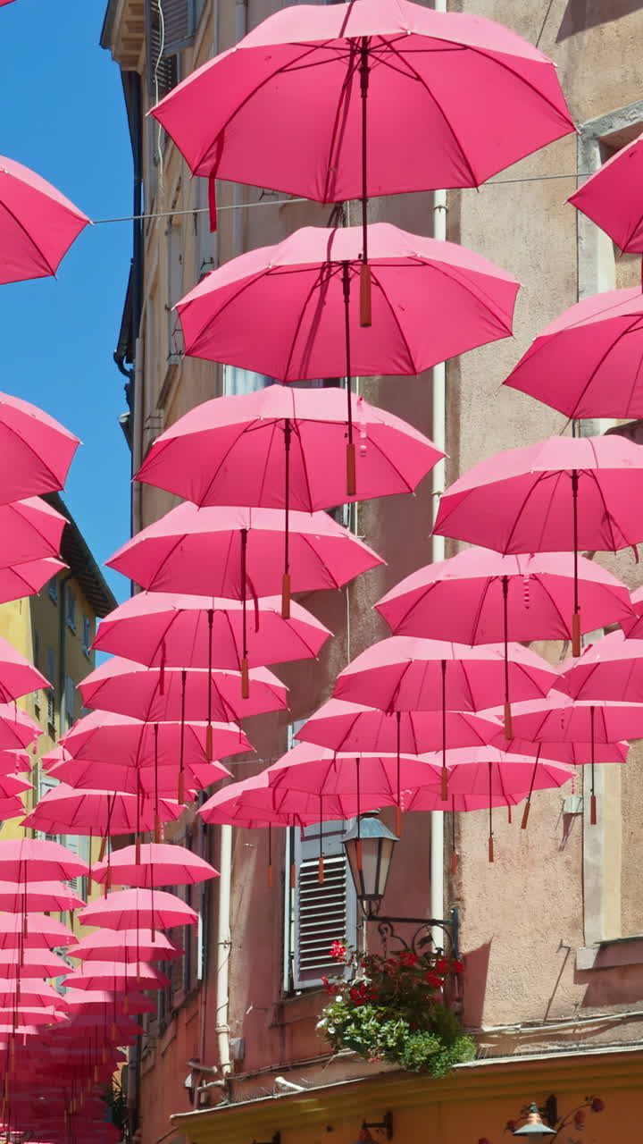 Rows of pink umbrellas above the streets of the old town in Grasse, France. Vertical