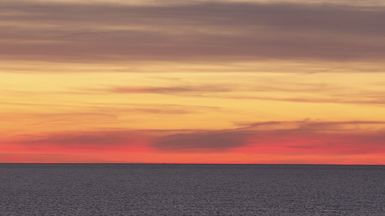 Colorful pastel orange yellow and pink hue sunset over the horizon, calm waters reflecting the vibrant sky in Estonia