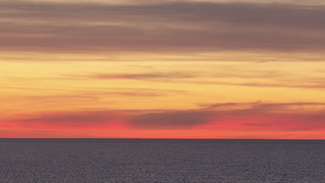 colorful pastel orange yellow and pink hue sunset over the horizon, calm waters reflecting the vibrant sky in estonia