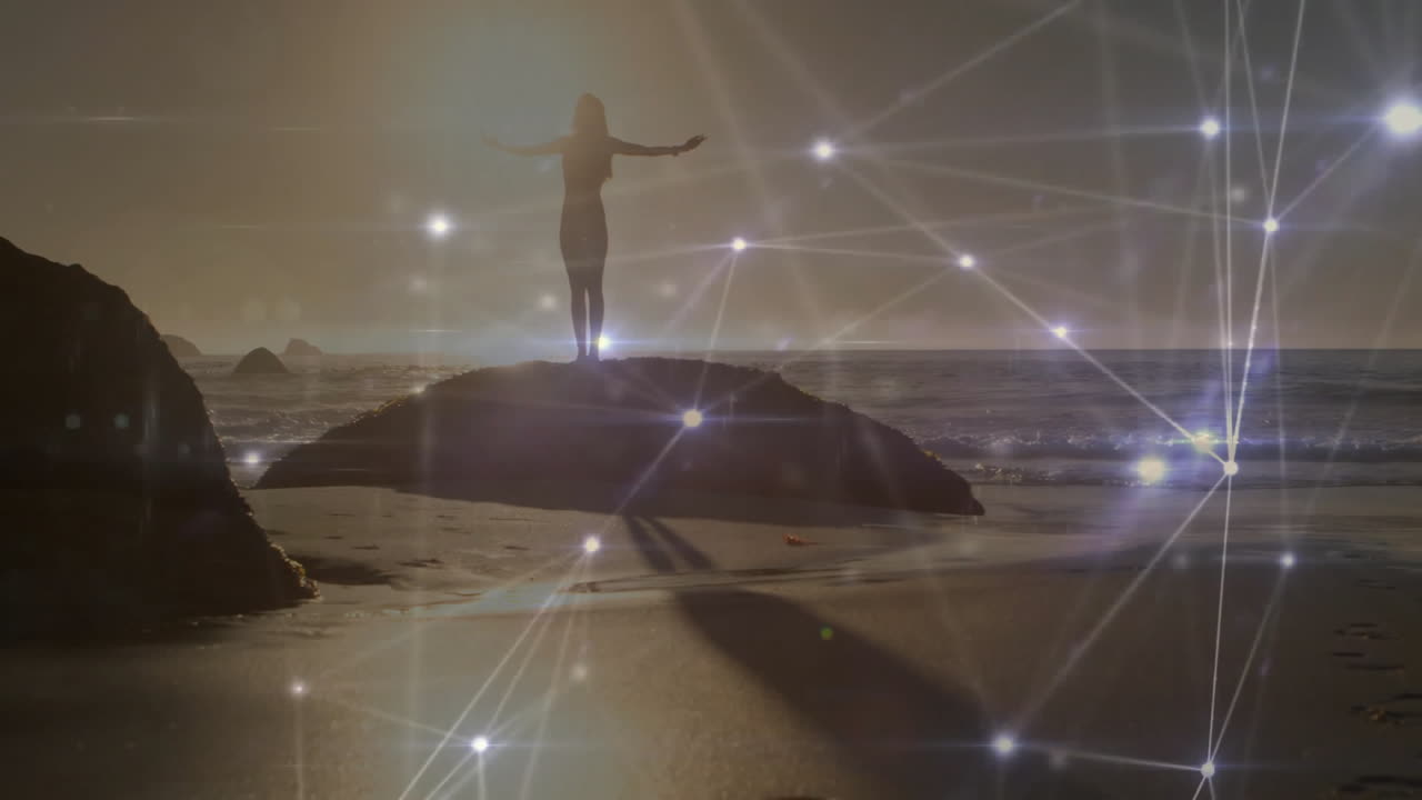 silhouetted woman stretching arms on rocky outcrop at sunset, showing technology network overlay