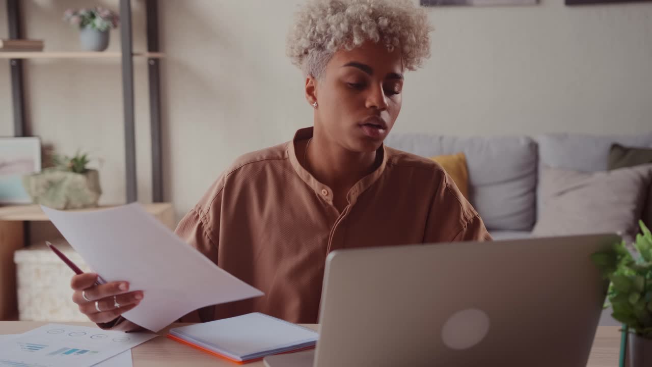 African female at home table reads reports compares data on paper and on laptop