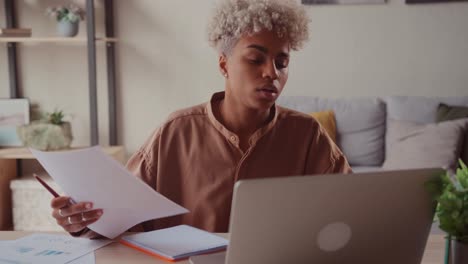african female at home table reads reports compares data on paper and on laptop