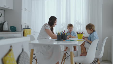 Two-children-of-boys-draw-with-his-mother-sitting-in-the-kitchen.