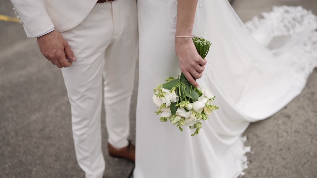 Brud med hvid blomsterbuket står ved siden af gom i lyst tøj, der viser bryllupsøjeblik og festdetaljer.