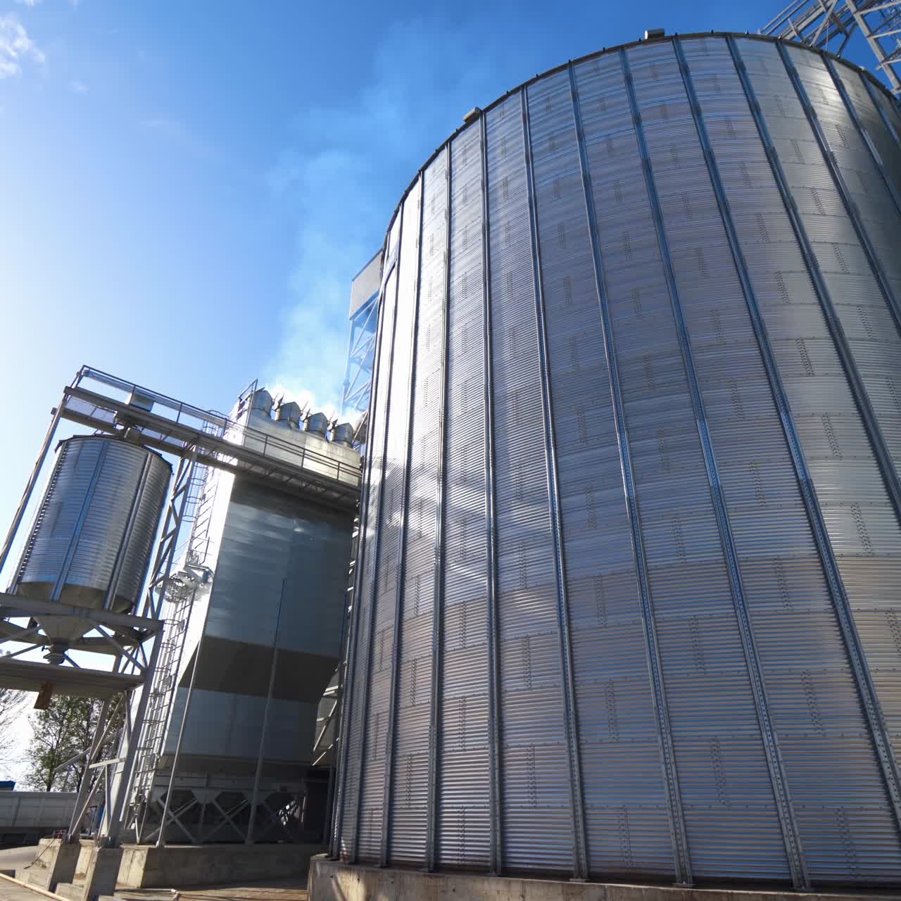 Modern grain elevators at bright sunny day. Large granary under blue sky. Industrial manufacturing in the open air