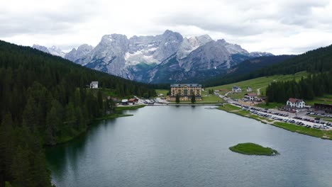 aerial dolly over lake misurina towards istituto pio xii rehabilitation centre with dolomite mountains in the background