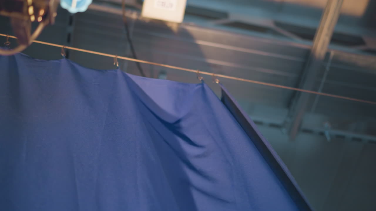 Overhead rigging suspends heavy blue curtain via metal clips on steel cables inside television studio, closeup view of ceiling grid and lighting hardware, backstage environment highlighting production