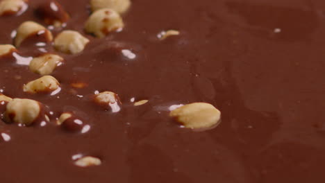 close up of hazelnuts being dropped into melted chocolate sauce