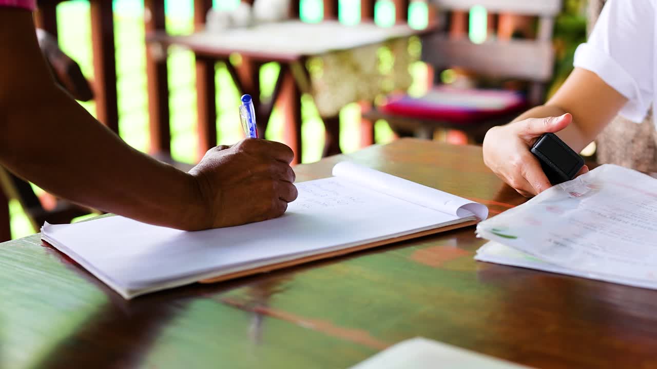 Two individuals collaborate on writing a food menu in a Phuket restaurant. Bright natural lighting enhances the focused, cooperative atmosphere