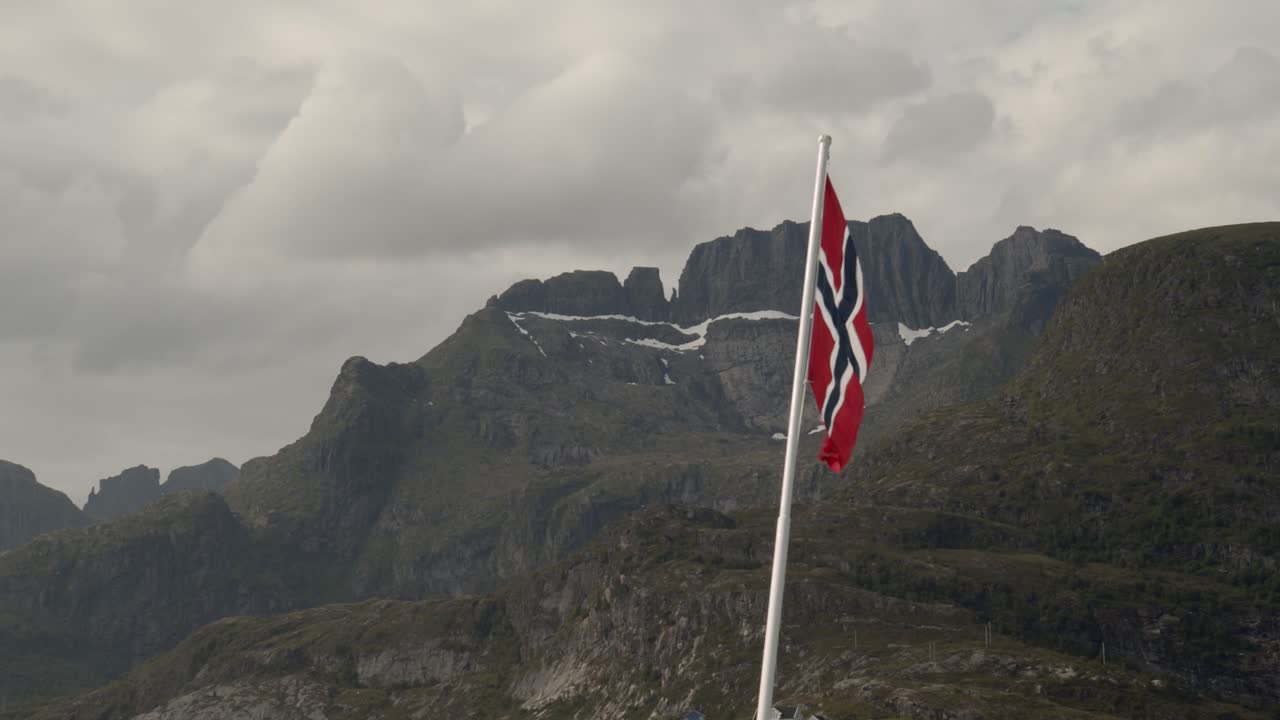 Bandiera della Norvegia che sventola al vento con le montagne delle Lofoten sullo sfondo.