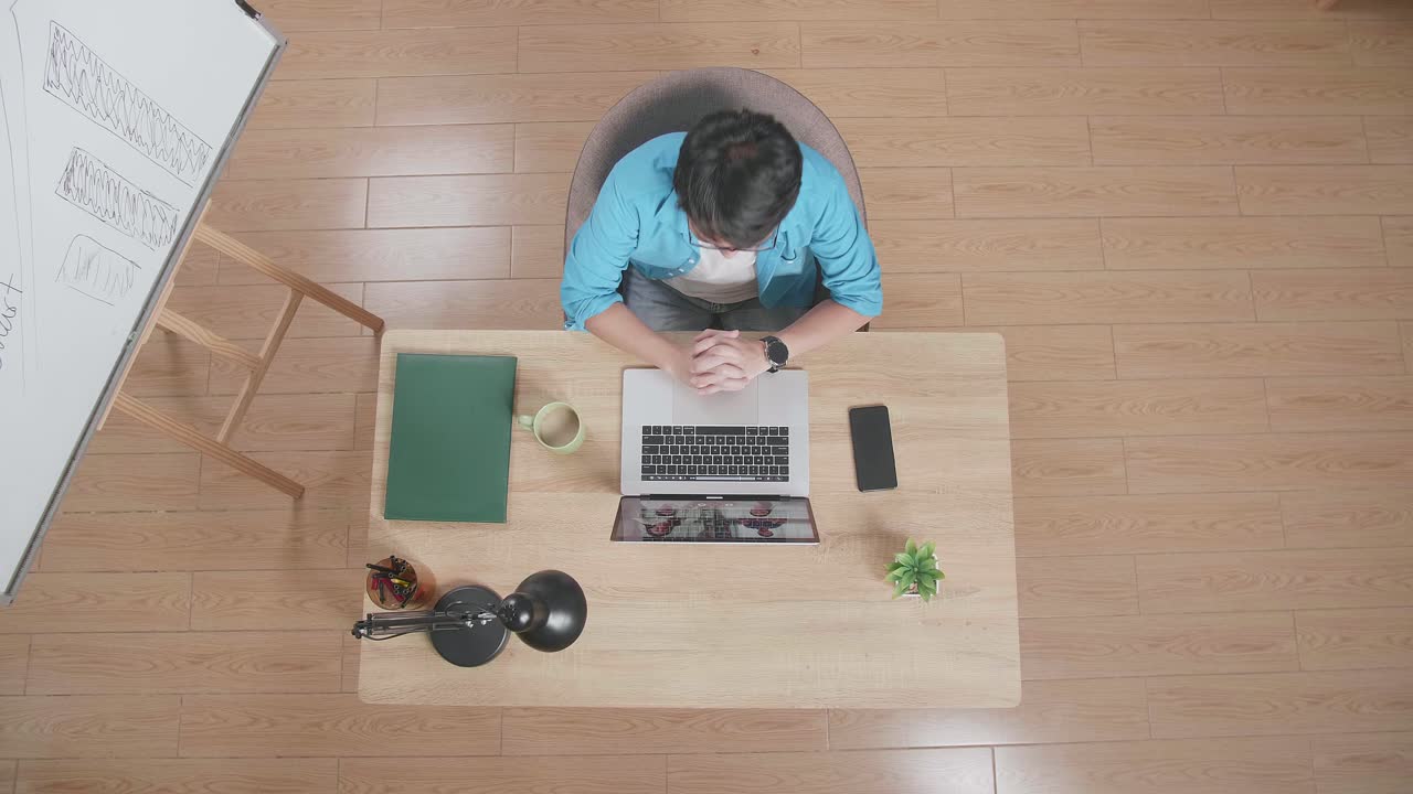 화이트 보드 에 나무 책상에 앉아서 손을 흔들고 있는 남자가 집에 있는 스마트폰 에 있는 노트북에서 회의를 하고 있다.