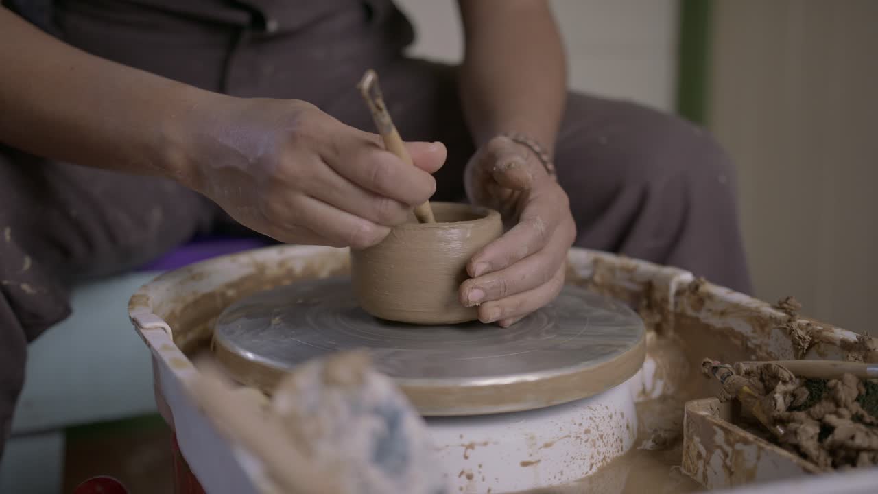Artesano dando forma a la arcilla en un torno de alfarero con herramientas, enfoque en las manos y la cerámica, taller interior
