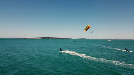 Professioneller-Wassersport-Kitesurfer,-Der-Bei-Schönem-Natürlichen-Nachmittagslicht-Mit-Blauem-Himmel-Und-Türkisfarbenem-Wasser-Auf-Offenem-Ozean-In-Kapstadt,-Südafrika,-Von-Einer-Drohne-Gejagt-Wird