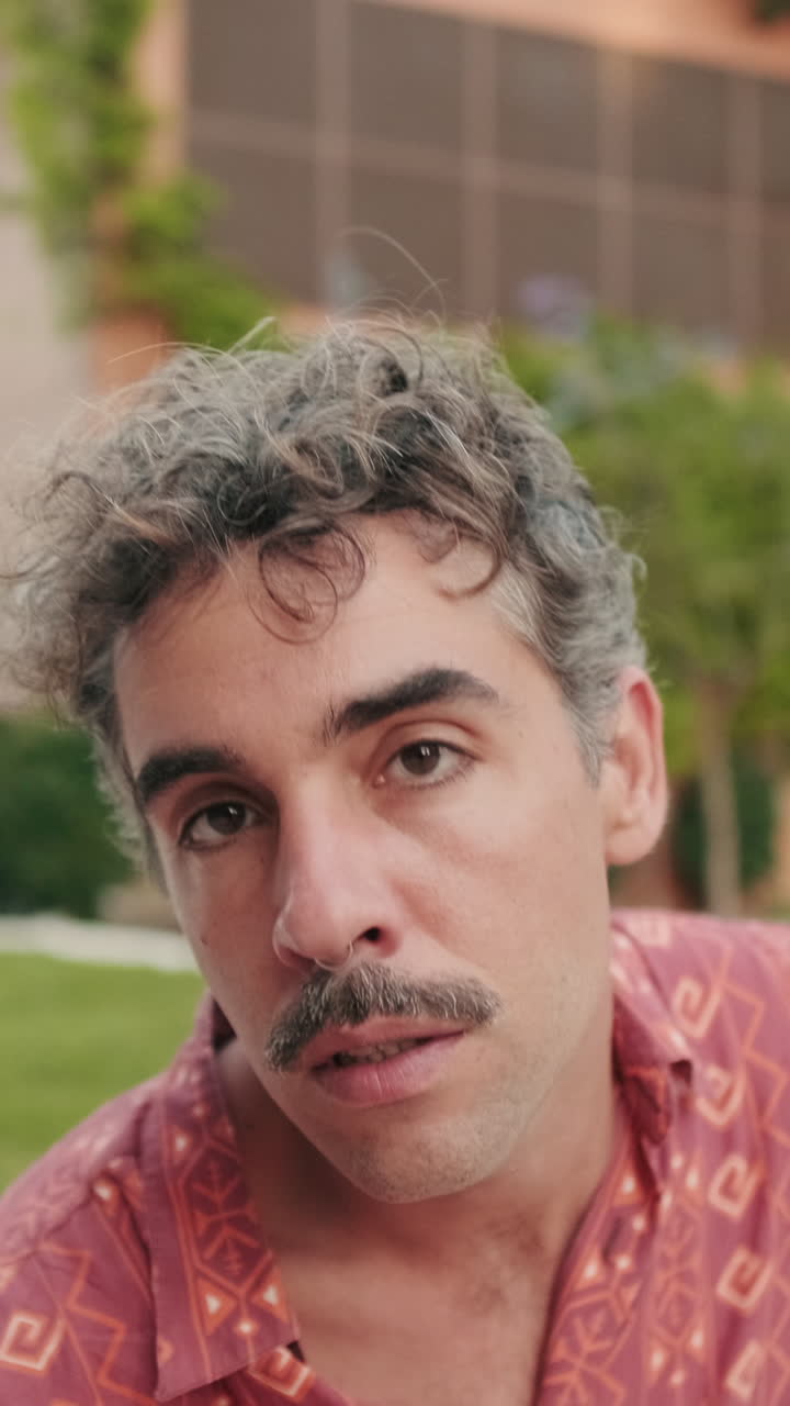 Uomo espressivo con capelli ricci e baffi che balla in un parco.