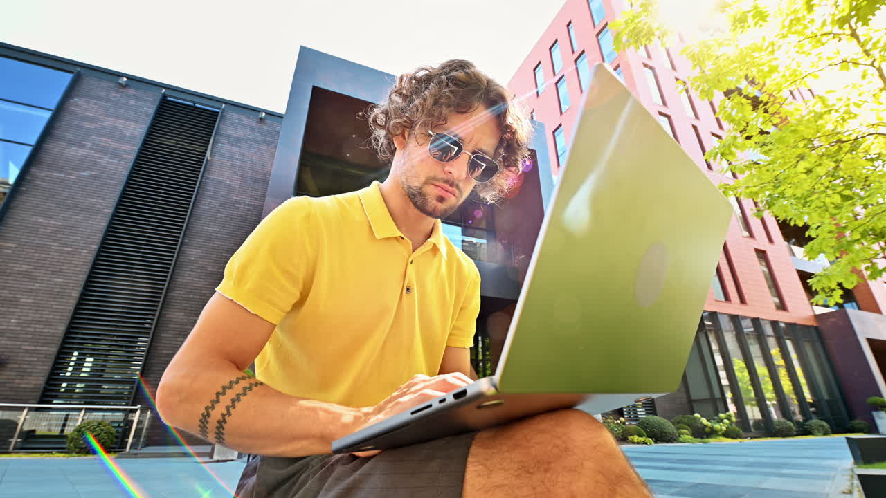 Man in yellow shirt talking standing on a bench and working on a laptop
