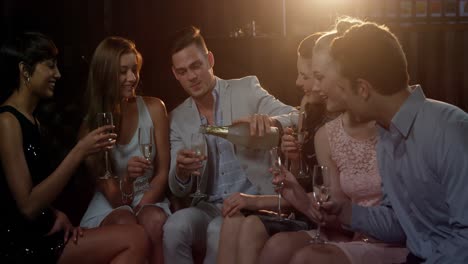 group of smiling friends sitting on sofa and toasting a glasses of champagne