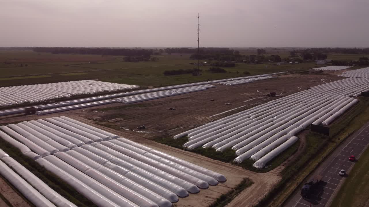 vista aérea de la maquinaria de trabajo en tierras agrícolas con bolsas de silo blancas durante el día nublado y soleado en américa del sur