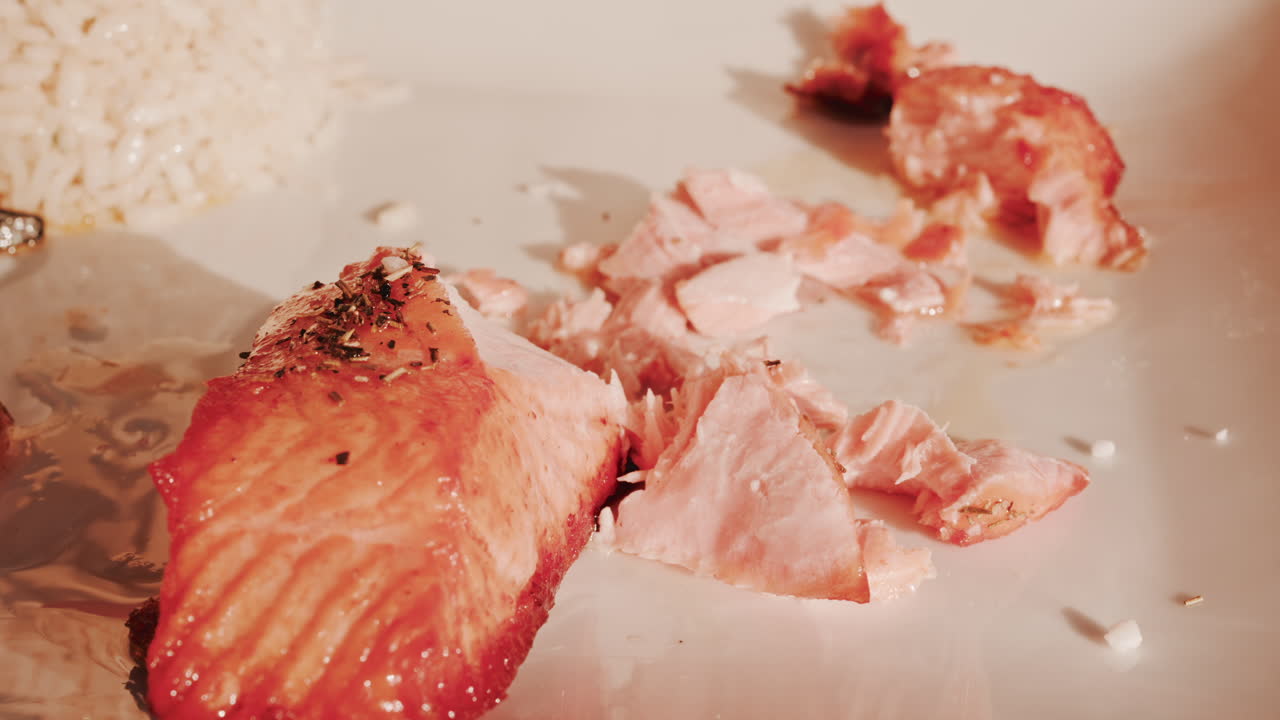 Close up of a fork and knife cutting into a a freshly grilled salmon fillet seasoned with herbs