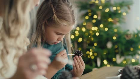 Focus-caucasian-woman-and-daughter-decorating-cone-with-white-paint.