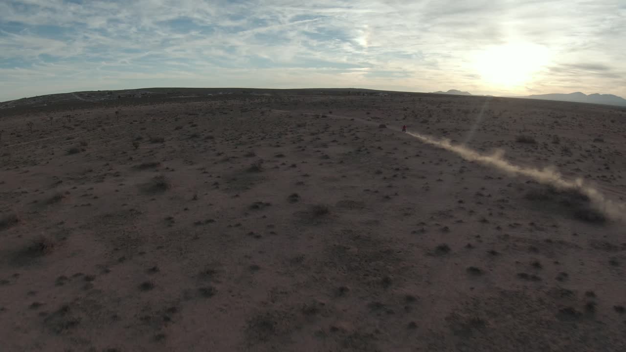 일몰 때 비포장 도로를 따라 모하비 사막을 질주하는 고독한 오토바이 - 공중 추격