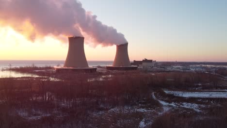 static aerial drone shot of nuclear power plant cooling towers at sunrise sunset with steam and smoke winter